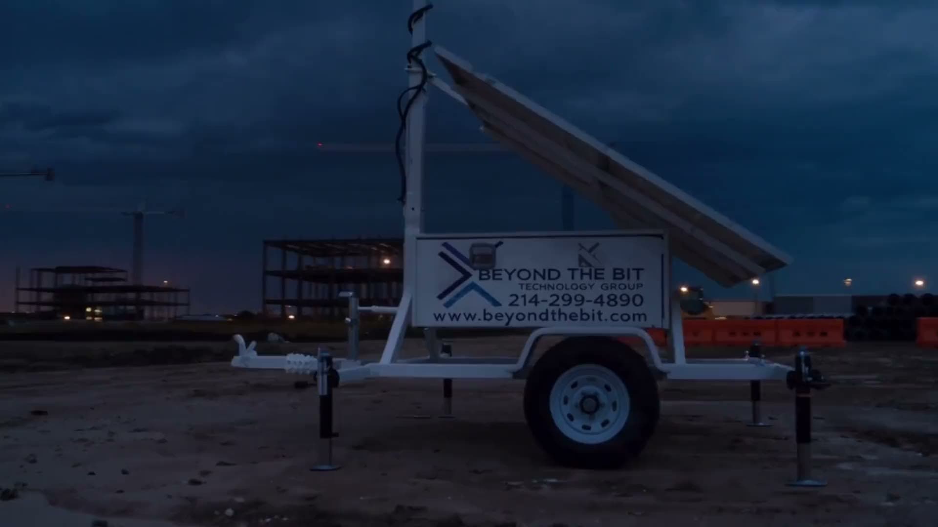 A Beyond the Bit security trailer with raised camera mast standing on a Dallas construction site at dusk, tower cranes and the skyline behind it.