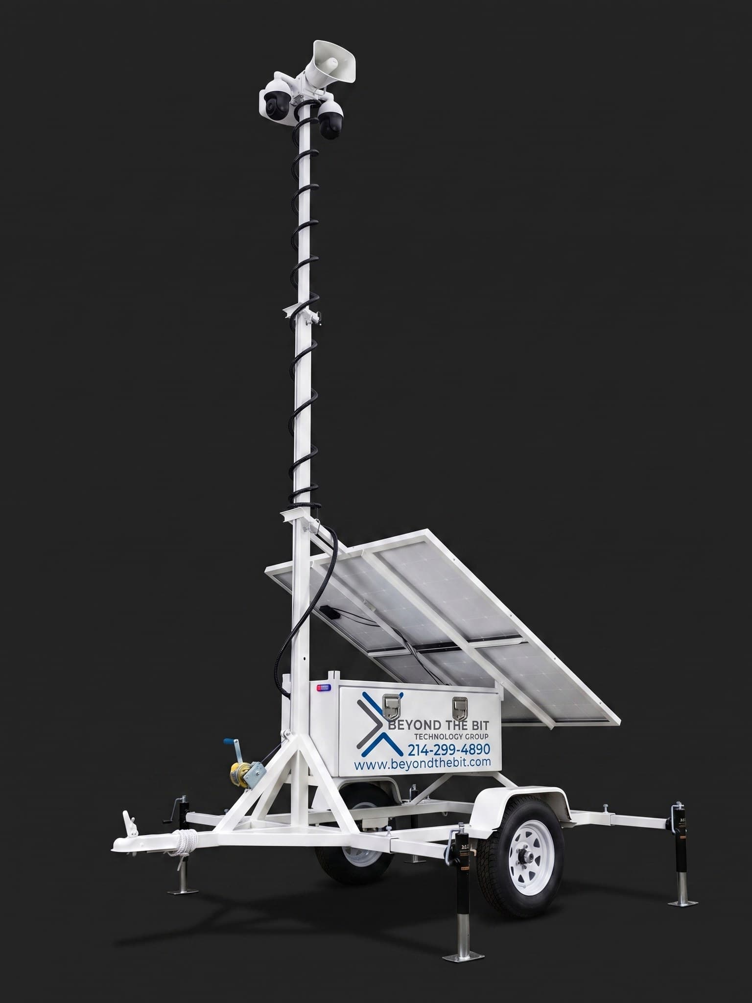 A Beyond the Bit security trailer photographed in a dark studio: white equipment box, fully raised telescoping camera mast, dual solar panels, and stabilizer jacks.